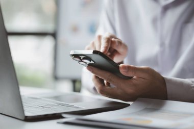 Business man looking at financial information from a mobile phone, he is checking company financial documents, he is an executive of a startup company. Concept of financial management.