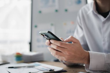 Business man looking at financial information from a mobile phone, he is checking company financial documents, he is an executive of a startup company. Concept of financial management.