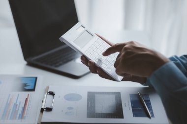 Bir şirketin mali belgelerindeki rakamları hesaplamak için hesap makinesi kullanan bir işadamı, şirketin nasıl büyüyeceğini planlamak için tarihsel finansal verileri analiz ediyor. Mali konsept.