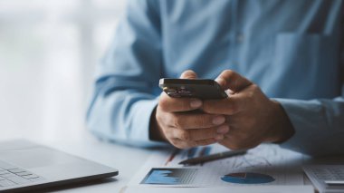 Business man looking at financial information from a mobile phone, he is checking company financial documents, he is an executive of a startup company. Concept of financial management.