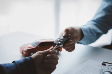 Bir araba kiralama şirketi çalışanı, kiracıyla kira sözleşmesini detaylar ve kiralama şartları hakkında konuştuktan sonra imzalaması gerektiğine işaret etti. Araba kiralama kavramı.