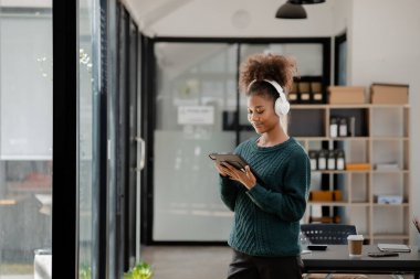 American woman standing with headphones in her room, she is resting and listening to music playing social chatting with friends. concept of relaxation.