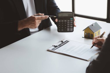 Bir kiralama şirketi çalışanı, kira sözleşmesi imzalamayı kabul eden müşterinin kira şartlarını ve koşullarını açıklayan maliyetini hesaplıyor. Ev ve gayrimenkul kiralama fikirleri.