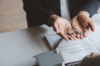 Bir ev kiralama şirketi çalışanı kira sözleşmesi imzalamayı kabul eden bir müşteriye kira sözleşmesinin detaylarını ve şartlarını açıklayan ev anahtarlarını teslim ediyor. Ev ve gayrimenkul kiralama fikirleri.