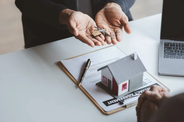 A home rental company employee is handing the house keys to a customer who has agreed to sign a rental contract, explaining the details and terms of the rental. Home and real estate rental ideas.