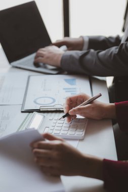 Bir şirketin mali belgelerindeki rakamları hesaplamak için hesap makinesi kullanan bir işadamı, şirketin nasıl büyüyeceğini planlamak için tarihsel finansal verileri analiz ediyor. Mali konsept.