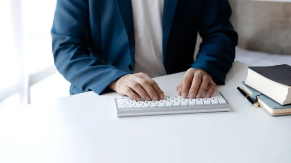 Person typing on a computer keyboard, businessman is working in a startup company's office, he is typing messages to his colleagues and making financial documents summarizing the meetings. Copy space.