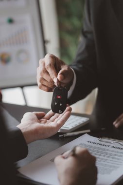 Bir araba kiralama şirketi çalışanı, kiracıyla kira sözleşmesini detaylar ve kiralama şartları hakkında konuştuktan sonra imzalaması gerektiğine işaret etti. Araba kiralama kavramı.