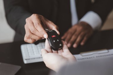 Bir araba kiralama şirketi çalışanı, kiracıyla kira sözleşmesini detaylar ve kiralama şartları hakkında konuştuktan sonra imzalaması gerektiğine işaret etti. Araba kiralama kavramı.