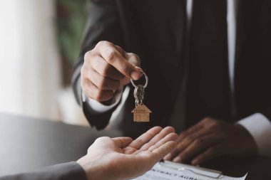 Bir ev kiralama şirketi çalışanı kira sözleşmesi imzalamayı kabul eden bir müşteriye kira sözleşmesinin detaylarını ve şartlarını açıklayan ev anahtarlarını teslim ediyor. Ev ve gayrimenkul kiralama fikirleri.