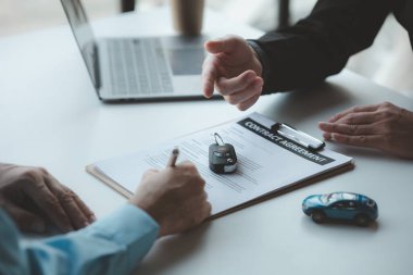 A car salesman is explaining the purchase details and details in the car purchase contract before signing acceptance of the terms, the car sales contract through an agent. Car trading concept.