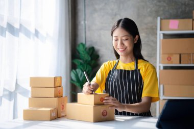 Online store salesperson is writing a customer's shipping address on parcel box before sending it to private carrier for delivery to customer. The idea of opening an online store and packing products.