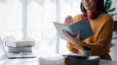 Asyalı genç bir kadın dizüstü bilgisayarla beyaz ofiste oturuyor, evde bilgisayarla internetten öğrenim görüyor, online internet eğitimi alıyor, internet üzerinden eğitim görüyor..