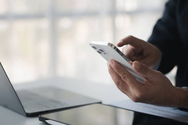Business man looking at financial information from a mobile phone, he is checking company financial documents, he is an executive of a startup company. Concept of financial management.