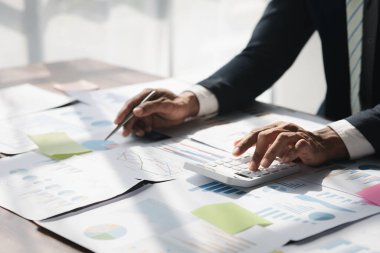 Bir şirketin mali belgelerindeki rakamları hesaplamak için hesap makinesi kullanan bir işadamı, şirketin nasıl büyüyeceğini planlamak için tarihsel finansal verileri analiz ediyor. Mali konsept.