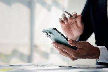 Business man looking at financial information from a mobile phone, he is checking company financial documents, he is an executive of a startup company. Concept of financial management.