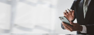 Business man looking at financial information from a mobile phone, he is checking company financial documents, he is an executive of a startup company. Concept of financial management.