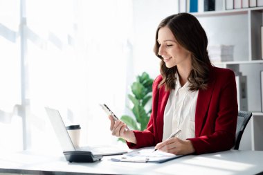 Cep telefonundan mali bilgilere bakan genç bir iş kadını, şirketin mali belgelerini kontrol ediyor, yeni kurulan bir şirketin kadın yöneticisidir. Mali yönetim kavramı.