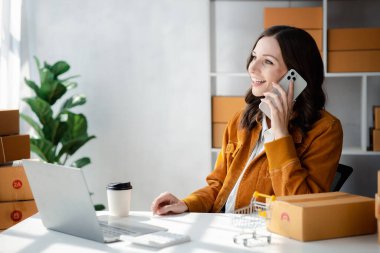 The woman is talking on the phone with a customer to confirm an order, she owns an online store, she packs and ships through a private transport company. Online selling and online shopping concepts.