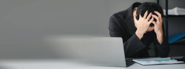 Businessman sitting in a company office, he is holding his head having a severe headache due to long hours of work and troubled work, sickness due to overwork. Office Syndrome.