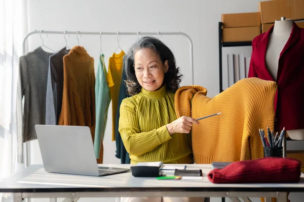 Elderly women are designers who make clothes, the owner of the shop, she is the owner of a female fashion clothing store and designs clothes and cutting the dress by herself, selling products online.