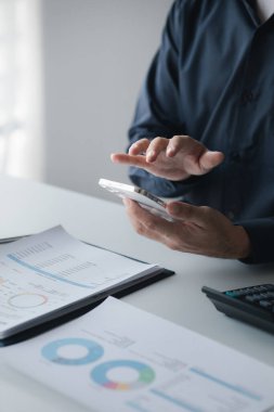 Business man looking at financial information from a mobile phone, he is checking company financial documents, he is an executive of a startup company. Concept of financial management.