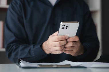 Business man looking at financial information from a mobile phone, he is checking company financial documents, he is an executive of a startup company. Concept of financial management.