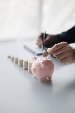 A businessman holding a coin in a piggy bank. Placing coins in a row from low to high is comparable to saving money to grow more. The concept of growing savings and saving by investing in stock funds.