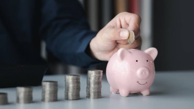 A businessman holding a coin in a piggy bank. Placing coins in a row from low to high is comparable to saving money to grow more. The concept of growing savings and saving by investing in stock funds.