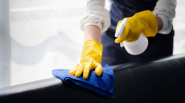 Person cleaning the room, cleaning staff is using cloth and spraying disinfectant to wipe the sofas in the company office room. Cleaning staff. Maintaining cleanliness in the organization.