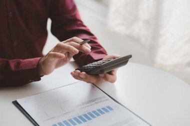 Businessman using a calculator to calculate numbers on a company's financial documents, he is analyzing historical financial data to plan how to grow the company. Financial concept.