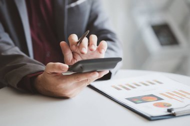 Businessman using a calculator to calculate numbers on a company's financial documents, he is analyzing historical financial data to plan how to grow the company. Financial concept.