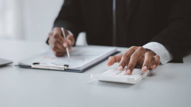 Bir işadamı finansal rakamları hesaplamak için beyaz hesap makinesi kullanıyor, özel ofisinde oturuyor, işadamı şirket finans tablosundaki mali verileri inceliyor..