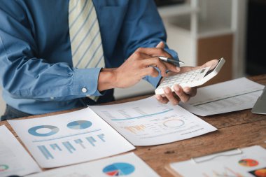Businessman using a calculator to calculate numbers on a company's financial documents, he is analyzing historical financial data to plan how to grow the company. Financial concept.