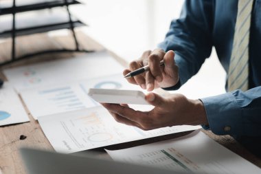 Businessman using a calculator to calculate numbers on a company's financial documents, he is analyzing historical financial data to plan how to grow the company. Financial concept.