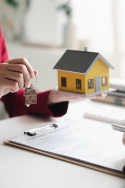 A home rental company employee is handing the house keys to a customer who has agreed to sign a rental contract, explaining the details and terms of the rental. Home and real estate rental ideas.