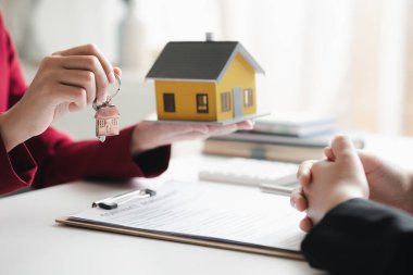 A home rental company employee is handing the house keys to a customer who has agreed to sign a rental contract, explaining the details and terms of the rental. Home and real estate rental ideas.
