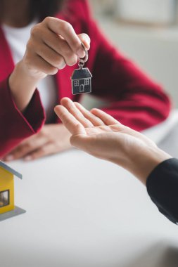 A home rental company employee is handing the house keys to a customer who has agreed to sign a rental contract, explaining the details and terms of the rental. Home and real estate rental ideas.