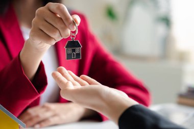 A home rental company employee is handing the house keys to a customer who has agreed to sign a rental contract, explaining the details and terms of the rental. Home and real estate rental ideas.