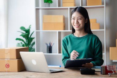 The owner of an online store is checking orders for packaged products in order to prepare them for delivery to customers as ordered through the website. Online selling and online shopping concepts.