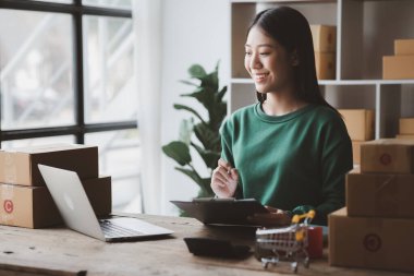 Bir çevrimiçi mağazanın sahibi, paketlenmiş ürünlerin siparişlerini web sitesinden sipariş edildiği gibi müşterilere teslimata hazırlamak için kontrol etmektedir. Çevrimiçi satış ve online alışveriş kavramları.