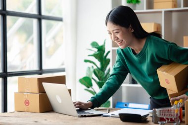 Bir çevrimiçi mağazanın sahibi, paketlenmiş ürünlerin siparişlerini web sitesinden sipariş edildiği gibi müşterilere teslimata hazırlamak için kontrol etmektedir. Çevrimiçi satış ve online alışveriş kavramları.