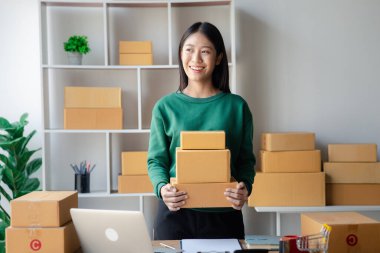 Bir çevrimiçi mağazanın sahibi, paketlenmiş ürünlerin siparişlerini web sitesinden sipariş edildiği gibi müşterilere teslimata hazırlamak için kontrol etmektedir. Çevrimiçi satış ve online alışveriş kavramları.