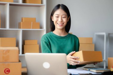 Bir çevrimiçi mağazanın sahibi, paketlenmiş ürünlerin siparişlerini web sitesinden sipariş edildiği gibi müşterilere teslimata hazırlamak için kontrol etmektedir. Çevrimiçi satış ve online alışveriş kavramları.