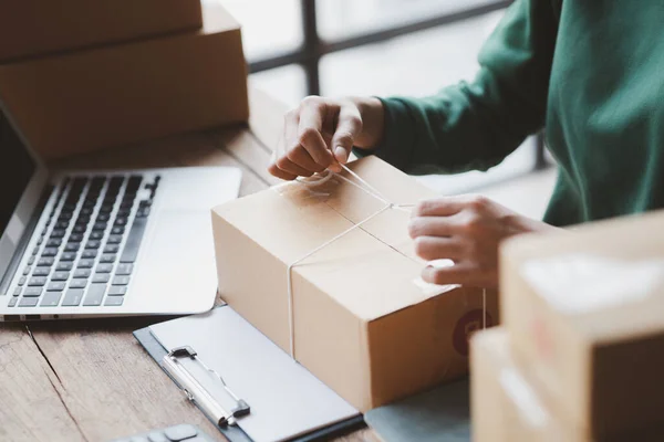 stock image An woman tying a parcel to a customer's box, she owns an online store, she packs and ships through a private transport company. Online selling and online shopping concepts.