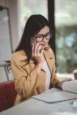 Asian woman talking on the phone, she is a salesperson in a startup company, she is calling customers to sell products and promotions. Concept of selling products through telephone channels.