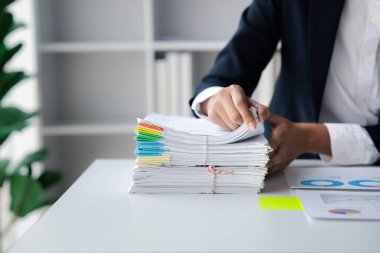 İşadamı masasında yığınla evrak, şirket finans belgeleri ve aylık mali özet kağıtlarını karıştırıyor. Organizasyondaki belge yönetimi kavramı.