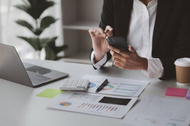 young businesswoman looking at financial information from a mobile phone, she is checking company financial documents, she is a female executive of a startup company. Concept of financial management.