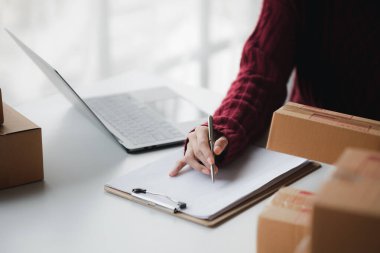 Bir kişi not defterine satış verileri yazıyor, çevrimiçi ürünler satıyor, online alışveriş sitelerinden sipariş veren müşterilerin siparişlerini paketliyor. Ürün çevrimiçi ve e-ticaret kavramı.