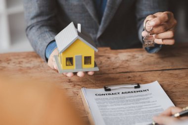 A home rental company employee is handing the house keys to a customer who has agreed to sign a rental contract, explaining the details and terms of the rental. Home and real estate rental ideas.